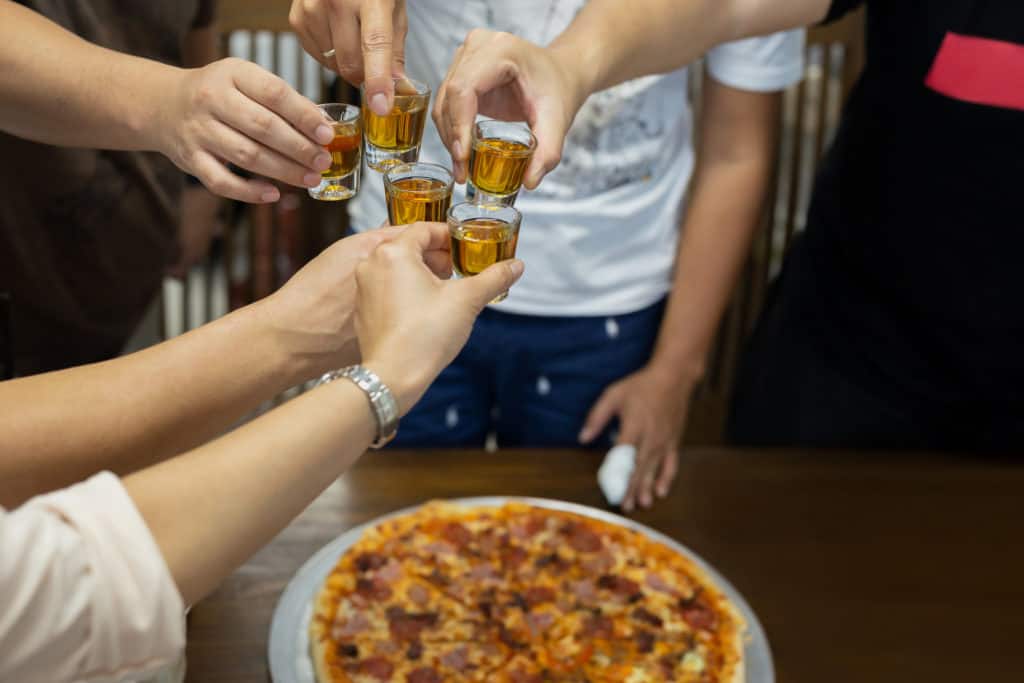 Friend with rum shots on party with pizza on table