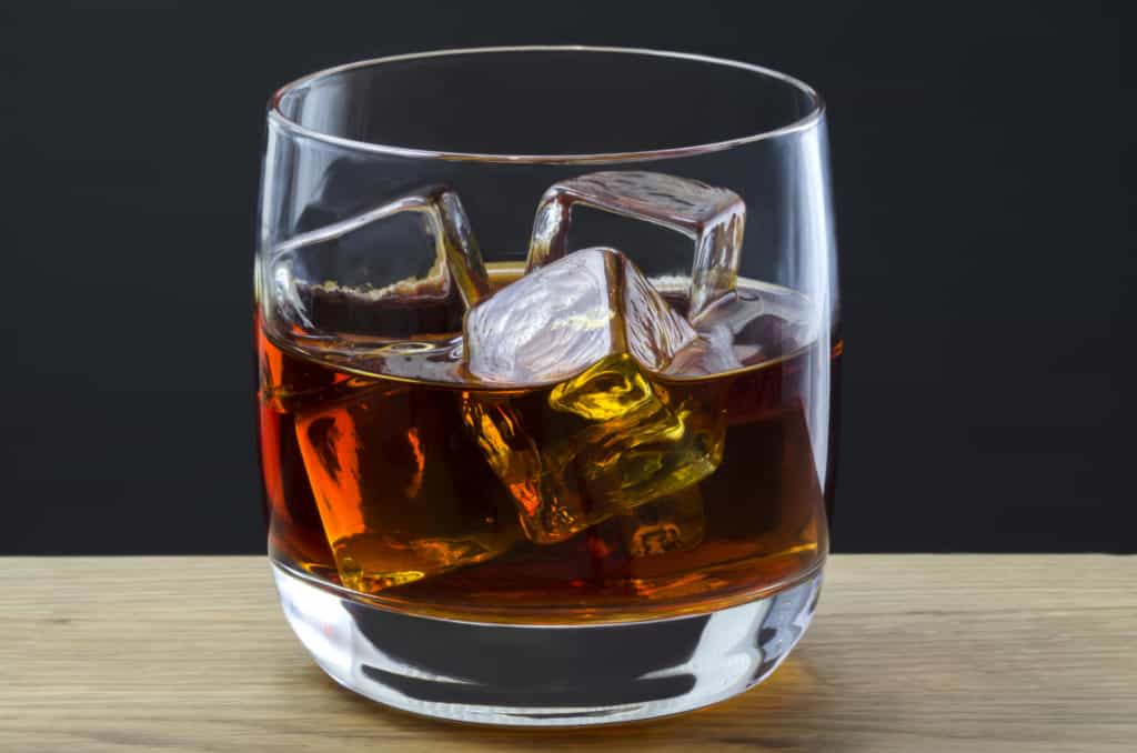 A large whiskey poured over ice cubes in a plain glass