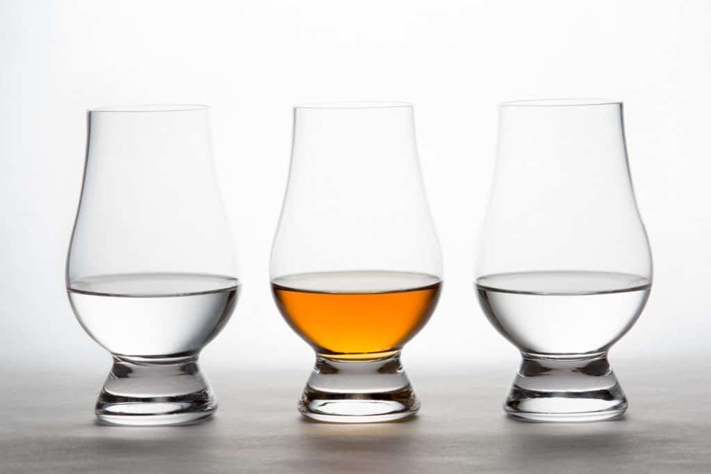Three backlit crystal glasses containing clear and amber liquor.  Vodka, whiskey, bourbon, brandy, etc.