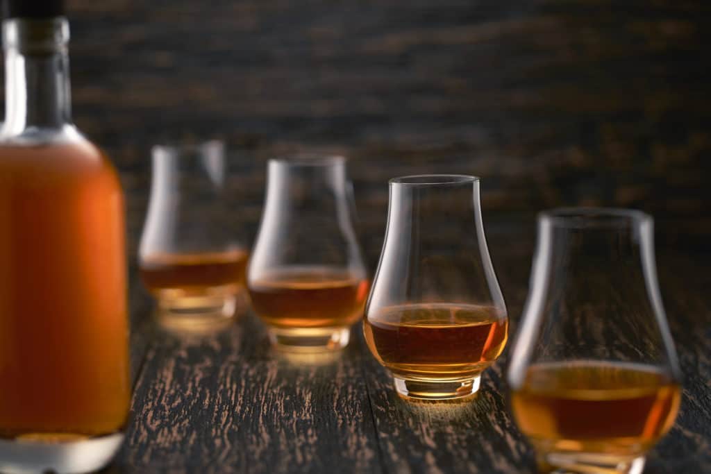 glasses of single malt whiskey on a wooden table with the silhouette of a bottle of whiskey.