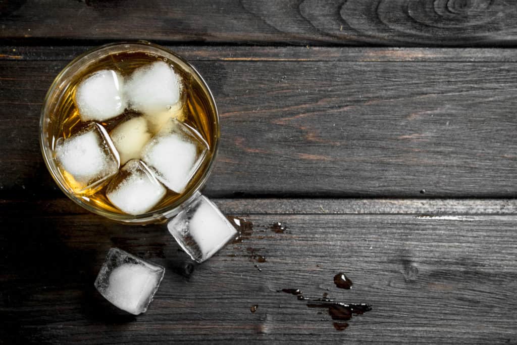 Whiskey in a glass with ice cubes. On wooden background