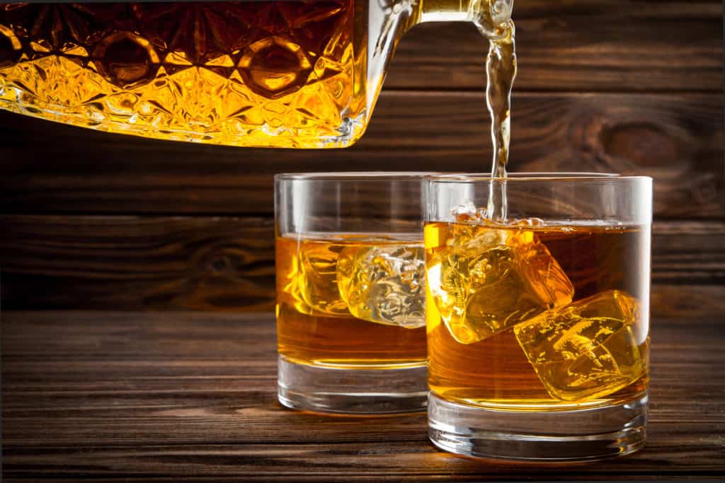 Pouring whiskey from bottle in the glasses on wooden background